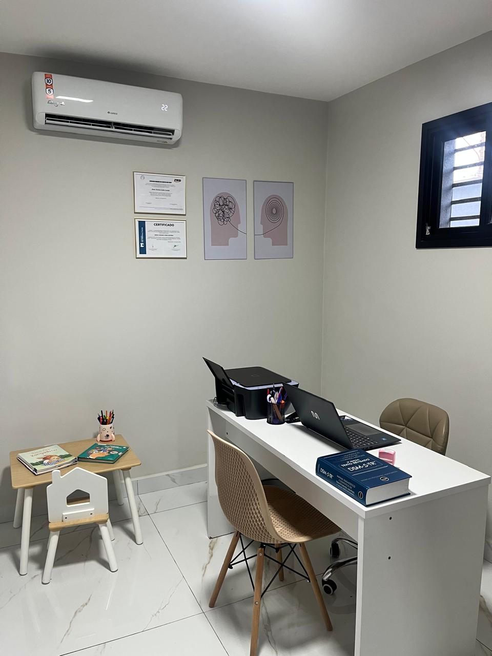 Sala de avaliação neuropsicológica com mesa, materiais, certificados e cantinho infantil