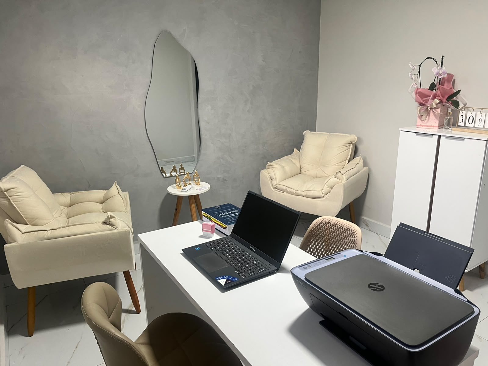 Sala de atendimento com poltrona clara, espelho orgânico e parede em cimento queimado