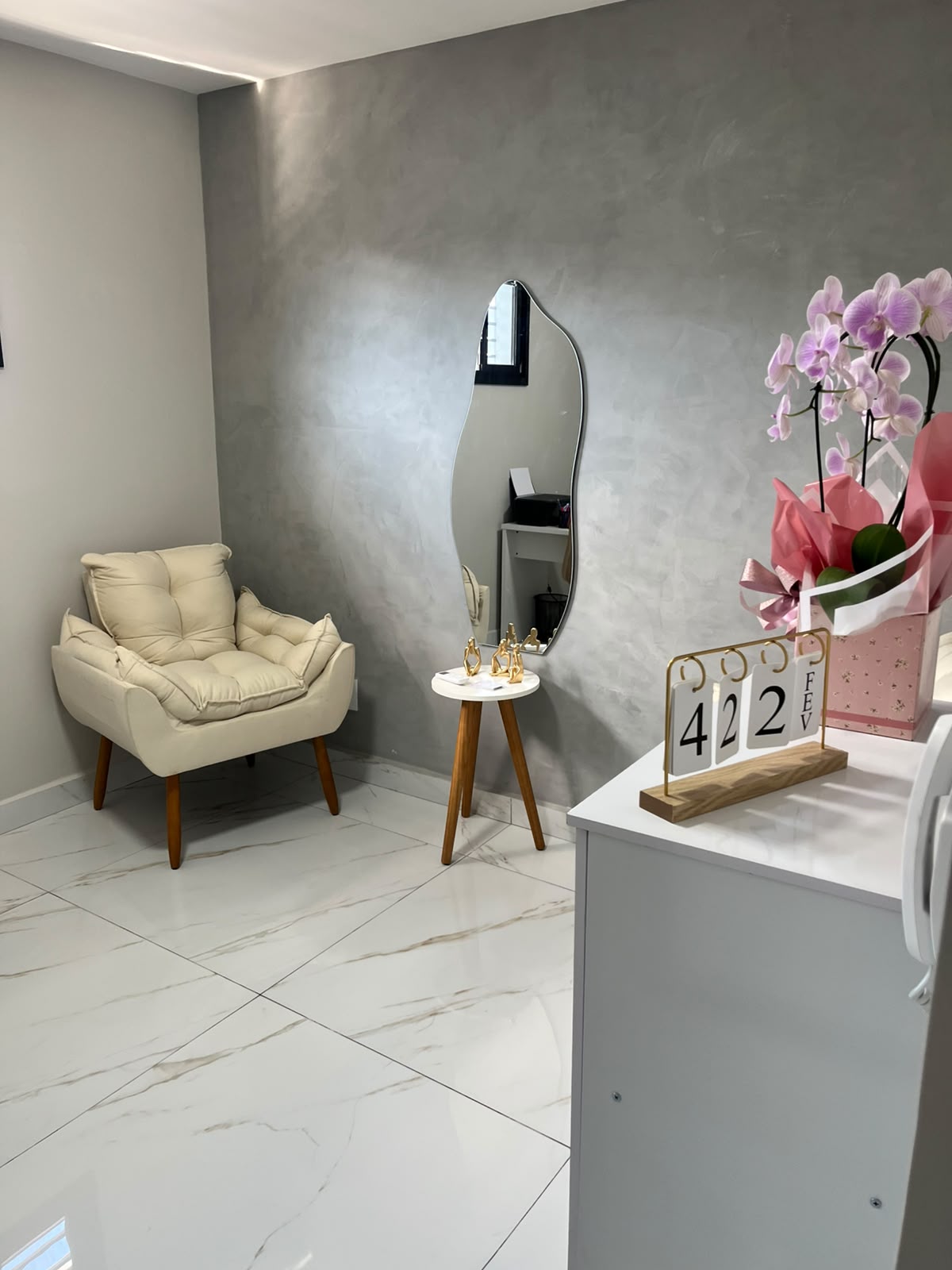 Sala de atendimento com poltrona clara, espelho orgânico e parede em cimento queimado